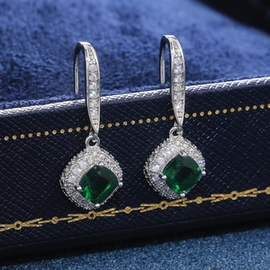 Macro view of cushion-cut emerald green zircon drop earrings in luxury velvet box