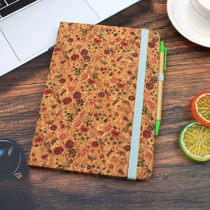 Detail of A5 cork notebook with floral patterns, elastic band, and matching green pen