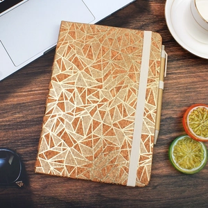 Flat lay of cork notebook with gold geometric pattern and matching pen on dark wood desk