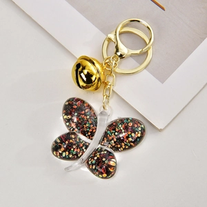 Detail of a black glitter butterfly charm with a gold bell on a keychain accessory