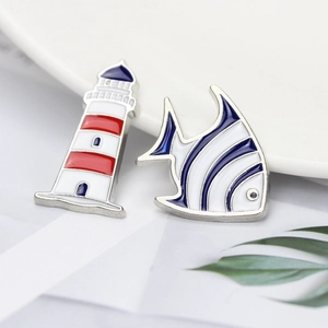Cartoon enamel pins featuring a nautical lighthouse and tropical fish in silver metal