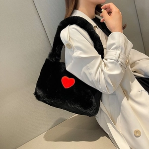 Stylish black plush shoulder bag with a red heart patch worn by a model in a trench coat