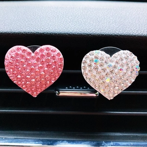 Macro detail of two heart-shaped car air vent clips with sparkling pink and colorful rhinestones