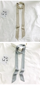 Detailed view of beige and grey narrow silk scarves laid flat on white textured fabric