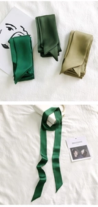 Detail of green silk-like scarf tied on a white handbag handle with natural lighting
