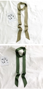Detail of olive and dark green satin skinny scarves on white textured fabric background