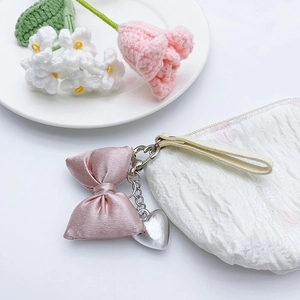 Pink satin bow keychain with silver heart charm on a white textured stylish handbag