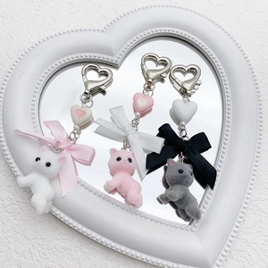 Three flocking kitten keychains with heart beads and satin bows on a white mirror surface