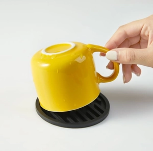 Macro detail of a yellow ceramic mug on a black round silicone drainage coaster pad