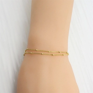 Detail of minimalist gold double-layered beaded chain bracelet on model's wrist