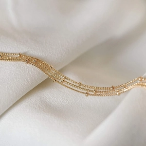 Detail of 14K gold plated layered bead bracelet on elegant white silk fabric