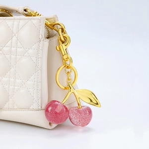 Pink glitter cherry keychain with gold leaves attached to a white quilted bag