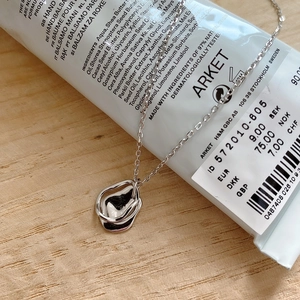 Detail of minimalist silver 925 irregular wavy pendant necklace over a cream tube