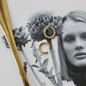 Golden beaded C-shaped cuff earrings in 18K gold plated stainless steel on editorial background