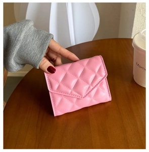 Close-up of a pink quilted PU leather wallet held over a wooden table setting