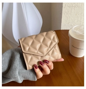 Close-up of a hand holding a khaki quilted leather mini wallet in a soft lifestyle setting