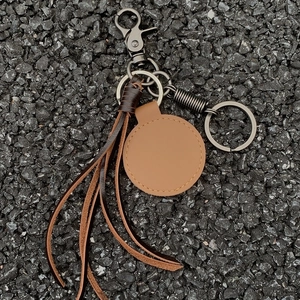 Handmade woven leather keychain with brown fringe and dark nickel clasp on stone surface