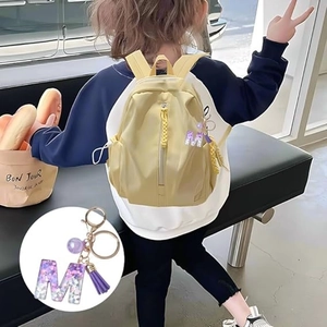 Sparkly purple glitter letter M keychain with tassel on a yellow backpack