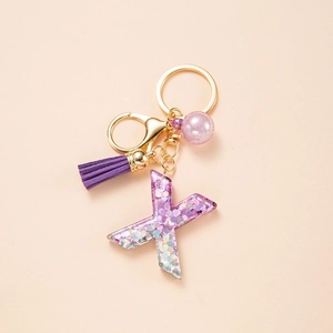 Macro view of purple glitter resin letter X keychain with gold clasp and tassel detail