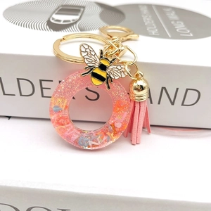 Close-up of pink resin letter O keychain with glitter, enamel bee, and leather tassel