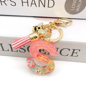 Close-up of pink resin S-shaped keychain with gold bee charm and leather tassel