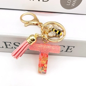 Detail of pink resin letter T keychain with glitter, metal bee charm and leather tassel