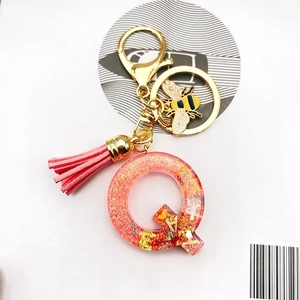 Detail of pink resin letter Q keychain with glitter, leather tassel and gold bee charm