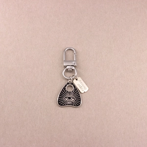 Detail of silver alloy keychain featuring a black planchette pendant with eye motif