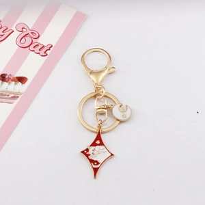 Detail showing a golden moon and cat charm keychain on a striped decorative card