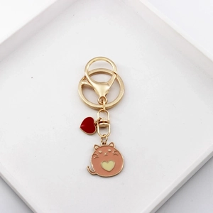 Detail view of a cute orange enamel cat keychain with heart charms on white tray