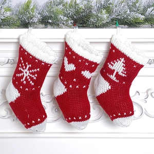 Three red and white knitted Christmas stockings with snowflake and tree patterns on mantel