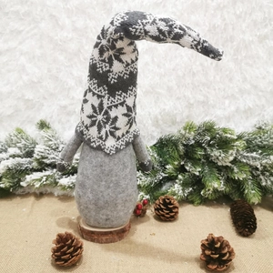 Detail of grey knitted Christmas gnome with snowflake pattern on a rustic wooden base