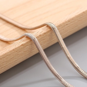 Macro shot of rose gold flat snake bone chain with polished metallic texture on wood