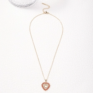 Golden heart pendant necklace featuring red and white cubic zirconia on a white surface