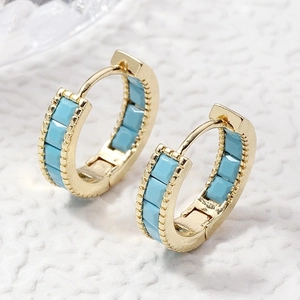 Golden earrings with sky blue stones and beaded texture on a white textured background