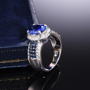 Macro detail of oval blue sapphire halo ring with pavé diamond band on velvet