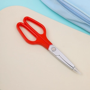 Close-up of portable red scissors with sharp silver metal blades and clear safety cap