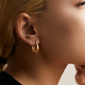 Close-up of a minimalist gold-plated U-shaped hoop earring worn on the earlobe