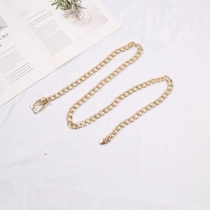 Detailed top view of a slim gold metal chain belt arranged in an S-shape on white fabric