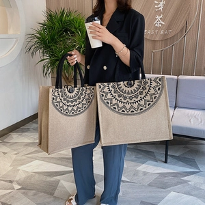 Detalle de bolsos de yute caqui con motivos étnicos negros portados por una modelo