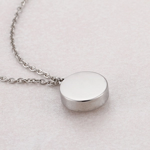 Polished silver titanium steel necklace featuring a thick round pendant on beige background