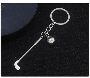 Close-up of a silver metal golf club and ball keychain on a dark textured surface