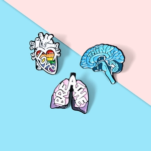 Dettaglio di tre spille in smalto con design creativo di cuore cervello e polmoni colorati