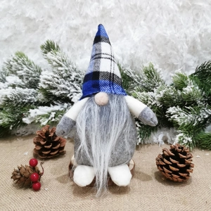 Close-up of Nordic Christmas gnome with blue plaid hat on wooden base and snowy pine decor
