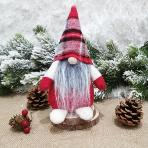 Close-up of Nordic Christmas gnome with plaid hat on wood base among pine cones
