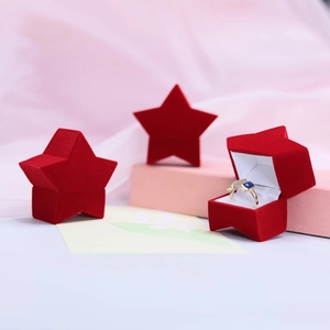 Three red velvet star-shaped jewelry boxes with gold ring on soft pink fabric