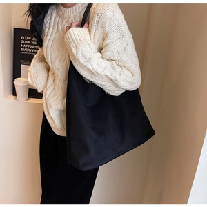 Close-up of minimalist black tote bag paired with a cable knit sweater and shoulder strap