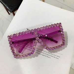 Close-up of purple oversized sunglasses with crystal rhinestones on a white book