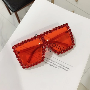Detail of oversized square sunglasses with red lenses and sparkling rhinestone frame