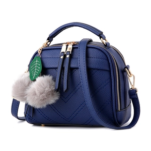 Blue shell crossbody bag with litchi texture, V-shaped stitching, and grey pompom charm